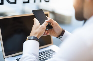 Nahaufnahme eines Geschäftsmannes mit Mobiltelefon und Laptop in einem Cafe - DIGF01234