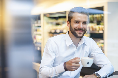 Lächelnder Geschäftsmann mit einer Tasse Kaffee in einem Kaffeehaus, lizenzfreies Stockfoto