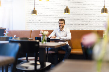 Lächelnder Geschäftsmann sitzt in einem Café mit einer Tasse Kaffee - DIGF01239
