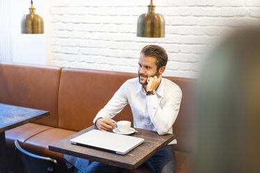 Smiling businessman sitting in a cafe with cup of coffee - DIGF01241