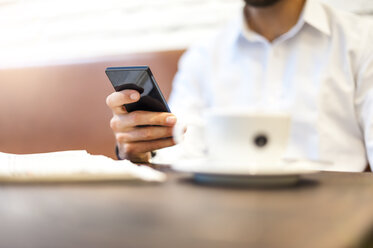 Nahaufnahme eines Geschäftsmannes mit Mobiltelefon und Tasse Kaffee in einem Cafe - DIGF01249