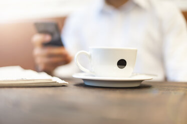 Nahaufnahme von Geschäftsmann Tasse Kaffee mit Geschäftsmann auf Handy im Hintergrund - DIGF01250