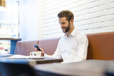 Smiling businessman looking at cell phone in a cafe - DIGF01251