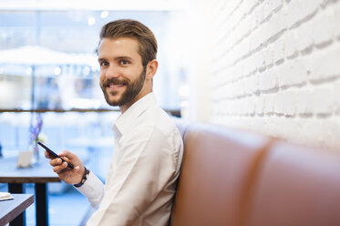 Smiling businessman with cell phone in a cafe - DIGF01254