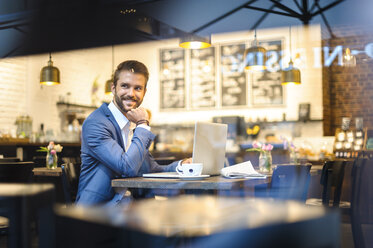 Smiling businessman with laptop in a cafe - DIGF01256