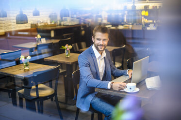 Smiling businessman with laptop in a cafe - DIGF01257