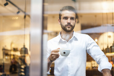 Geschäftsmann hält eine Tasse Kaffee und schaut durch ein Fenster - DIGF01267
