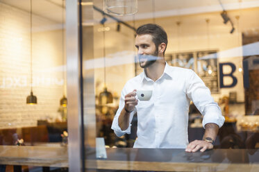 Lächelnder Geschäftsmann hält eine Tasse Kaffee hinter einer Fensterscheibe in einem Café - DIGF01268