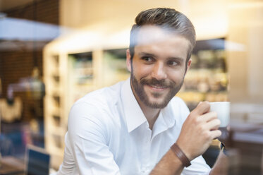 Lächelnder Geschäftsmann hält eine Tasse Kaffee hinter einer Fensterscheibe in einem Café - DIGF01271