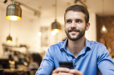 Lächelnder junger Mann mit Mobiltelefon in einem Cafe - DIGF01282