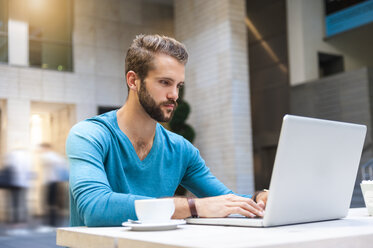 Junger Mann sitzt am Tisch und benutzt einen Laptop - DIGF01294