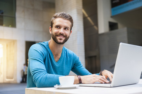 Smiling young man sitting at table using laptop stock photo