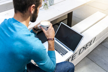 Businessman sitting on bench analyzing data on laptop display - DIGF01299