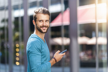 Lächelnder junger Mann mit Mobiltelefon in der Stadt - DIGF01307