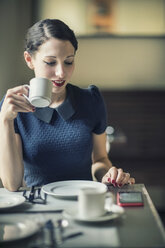 Junge Frau schaut auf ein Handy in einem Café - TAMF00660