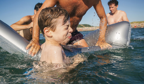 Drei Männer und ein Junge haben Spaß mit Luftmatratze im Meer, lizenzfreies Stockfoto