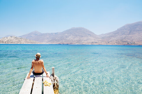 Greece, Cyclades islands, Amorgos, man sitting on the edge of a wooden pier, Nikouria island - GEMF01020