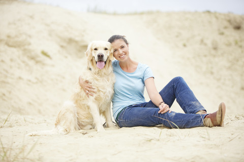 Lächelnde junge Frau mit Hund im Sand, lizenzfreies Stockfoto