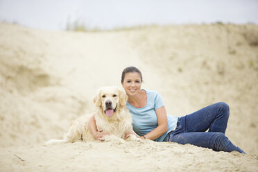 Lächelnde junge Frau mit Hund im Sand - MAEF12031