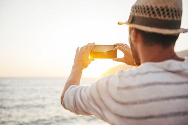 Greece, Cylcades Islands, Amorgos, man taking pictures of the sunset with a smartphone next to the sea - GEMF01033