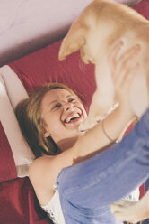 Happy young woman lying on bed playing with her Labrador Retriever puppy - SKCF00202