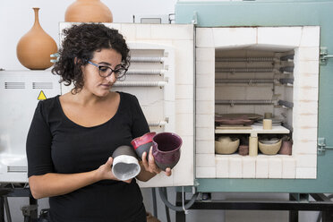 Woman examining cups of ceramic in a workshop - ABZF01242