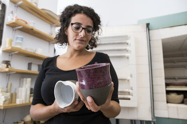 Woman examining cups of ceramic in a workshop - ABZF01243