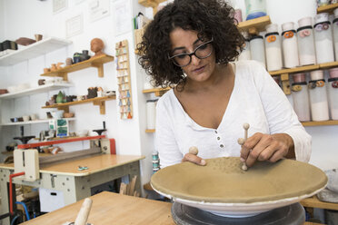 Woman decorating a plate in a ceramics workshop - ABZF01247