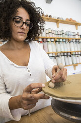 Woman decorating a plate in a ceramics workshop - ABZF01248