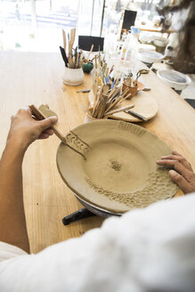 Frau dekoriert einen Teller in einer Keramikwerkstatt - ABZF01249