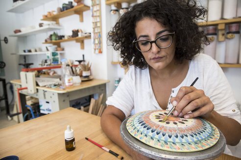 Woman painting a ceramic plate with a brush - ABZF01251