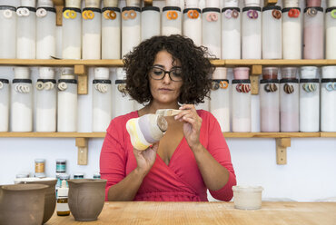 Frau bemalt eine Keramiktasse mit einem Pinsel in ihrer Werkstatt - ABZF01255