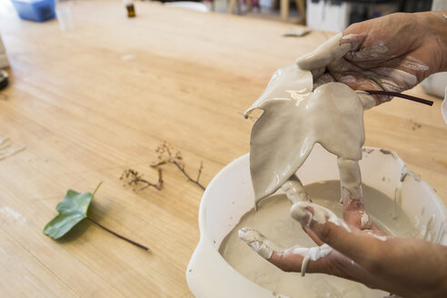 Hands holding a porcelain leaf after inmersing it in liquid porcelain - ABZF01258