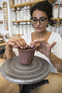 Woman sculpting a cup with clay in a ceramic workshop - ABZF01261