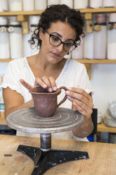 Woman placing the handle of a cup of clay in a ceramic workshop - ABZF01262