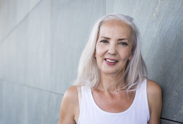 Porträt einer lächelnden Frau mit grauem Haar, die sich an eine Wand lehnt - JUNF00624
