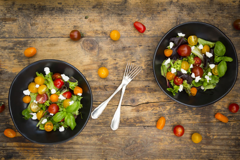 Zwei Schalen Blattsalat mit Ziegenfrischkäse und Tomaten auf Holz, lizenzfreies Stockfoto