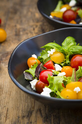 Bowl of leaf salad with goat cream cheese and tomatoes on wood - LVF05340