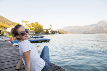 Austria, Sankt Wolfgang, smiling woman sitting on jetty at lake - JUNF00627