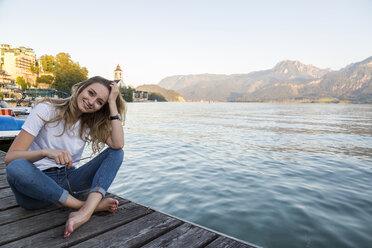 Austria, Sankt Wolfgang, smiling woman sitting on jetty at lake - JUNF00628