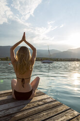 Österreich, Sankt Wolfgang, Frau im Bikini in Yoga-Pose auf Steg am See sitzend - JUNF00639