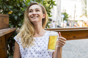 Happy woman with beer mug in a street restaurant looking up - JUNF00651