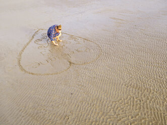 Woman at the beach drawing heart into the wet sand - LAF01748