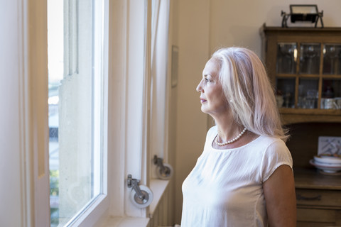 Reife Frau schaut durch das Fenster zu Hause, lizenzfreies Stockfoto