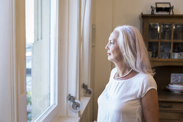 Mature woman looking through window at home - JUNF00664