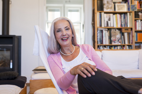 Lachende Frau in einem Sessel zu Hause sitzend, lizenzfreies Stockfoto
