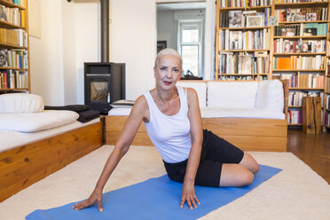 Porträt einer Frau, die auf einer Gymnastikmatte im Wohnzimmer sitzt - JUNF00696