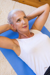 Porträt einer Frau, die auf einer Gymnastikmatte im Wohnzimmer trainiert - JUNF00701