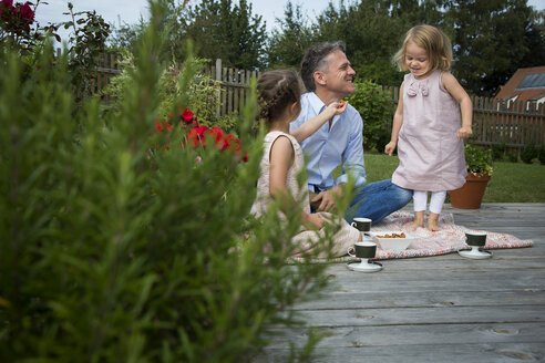 Father drinking tea with his daughters in the garden - JTLF00113