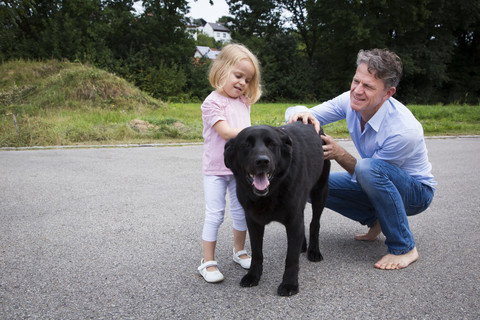 Vater und Tochter streicheln Hund im Garten, lizenzfreies Stockfoto